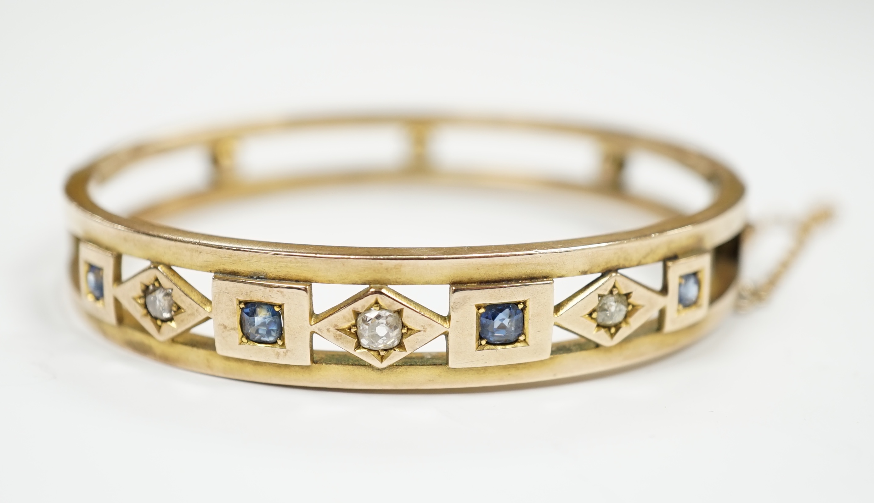 An Edwardian yellow metal, sapphire and diamond set hinged bangle, interior diameter 55mm, gross weight 14.4 grams, with box.